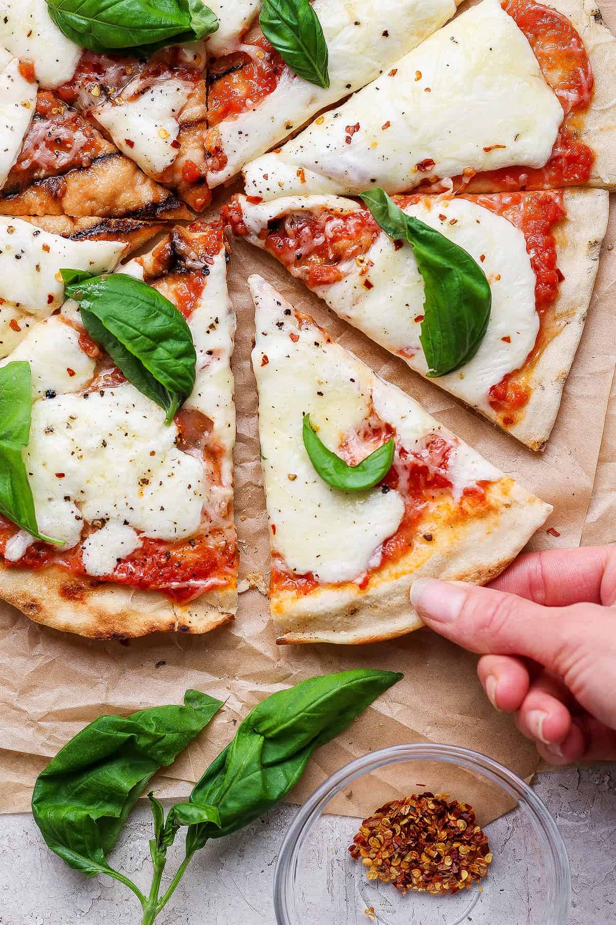 This Grilled Pizza recipe is tested and perfected, with a homemade dough that doesn't fall through the grates. Smoky, crispy, and delicious! Hand pulling slice of grilled Margherita pizza from pie.