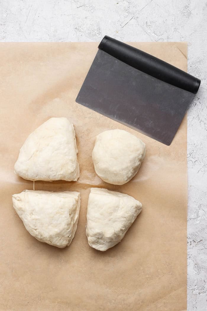 This Grilled Pizza recipe is tested and perfected, with a homemade dough that doesn't fall through the grates. Smoky, crispy, and delicious! Dough divided into 4 portions with bench scraper.