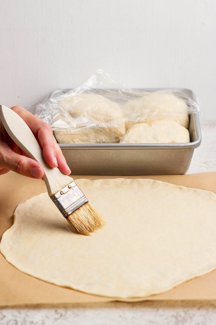 This Grilled Pizza recipe is tested and perfected, with a homemade dough that doesn't fall through the grates. Smoky, crispy, and delicious! Brushing oil onto dough for pizza crust.