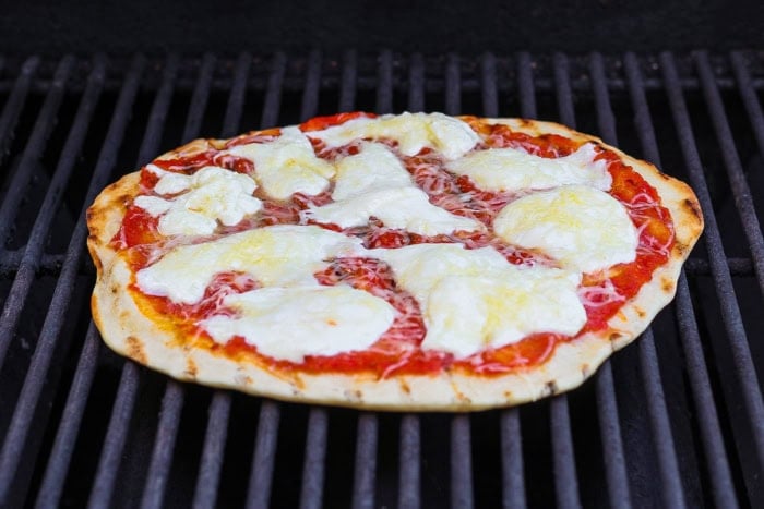 This Grilled Pizza recipe is tested and perfected, with a homemade dough that doesn't fall through the grates. Smoky, crispy, and delicious! Pizza cooking on grill.
