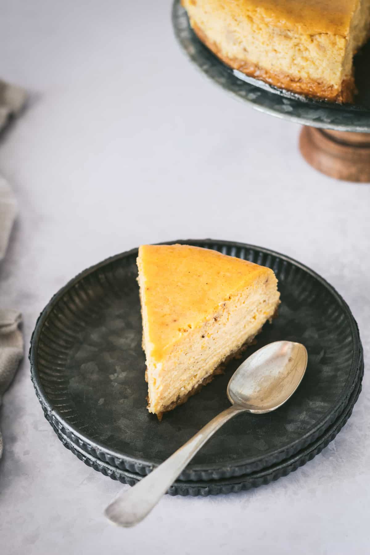 A slice of pumpkin cheesecake with gingersnap crust on a plate with a spoon