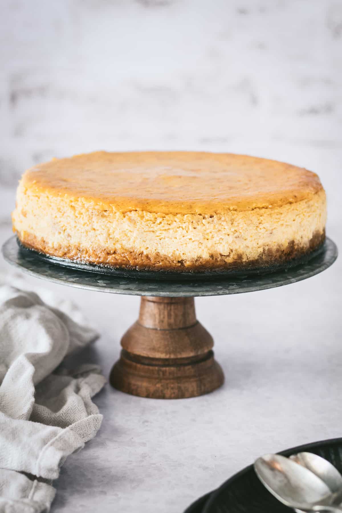 Creamy pumpkin cheesecake with gingersnap crust on a serving stand
