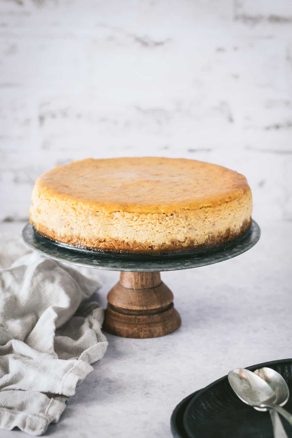 Creamy pumpkin cheesecake with gingersnap crust on a serving stand