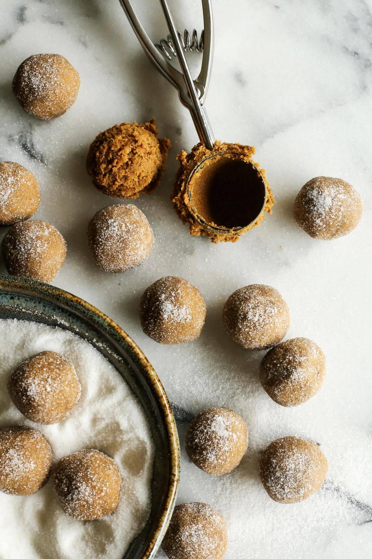 a cookie scoop and balls of cookie dough rolled in sugar