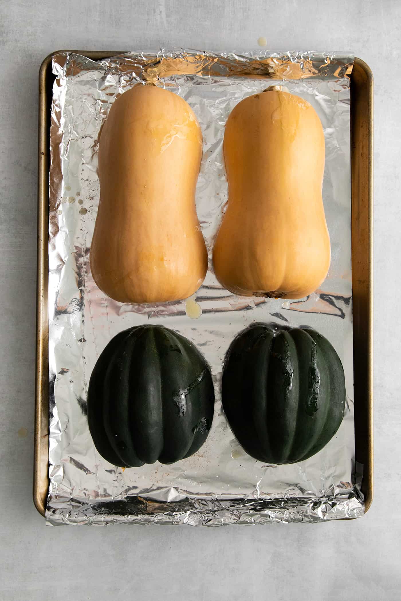 A butternut squash and acorn squash cut in half on a baking sheet