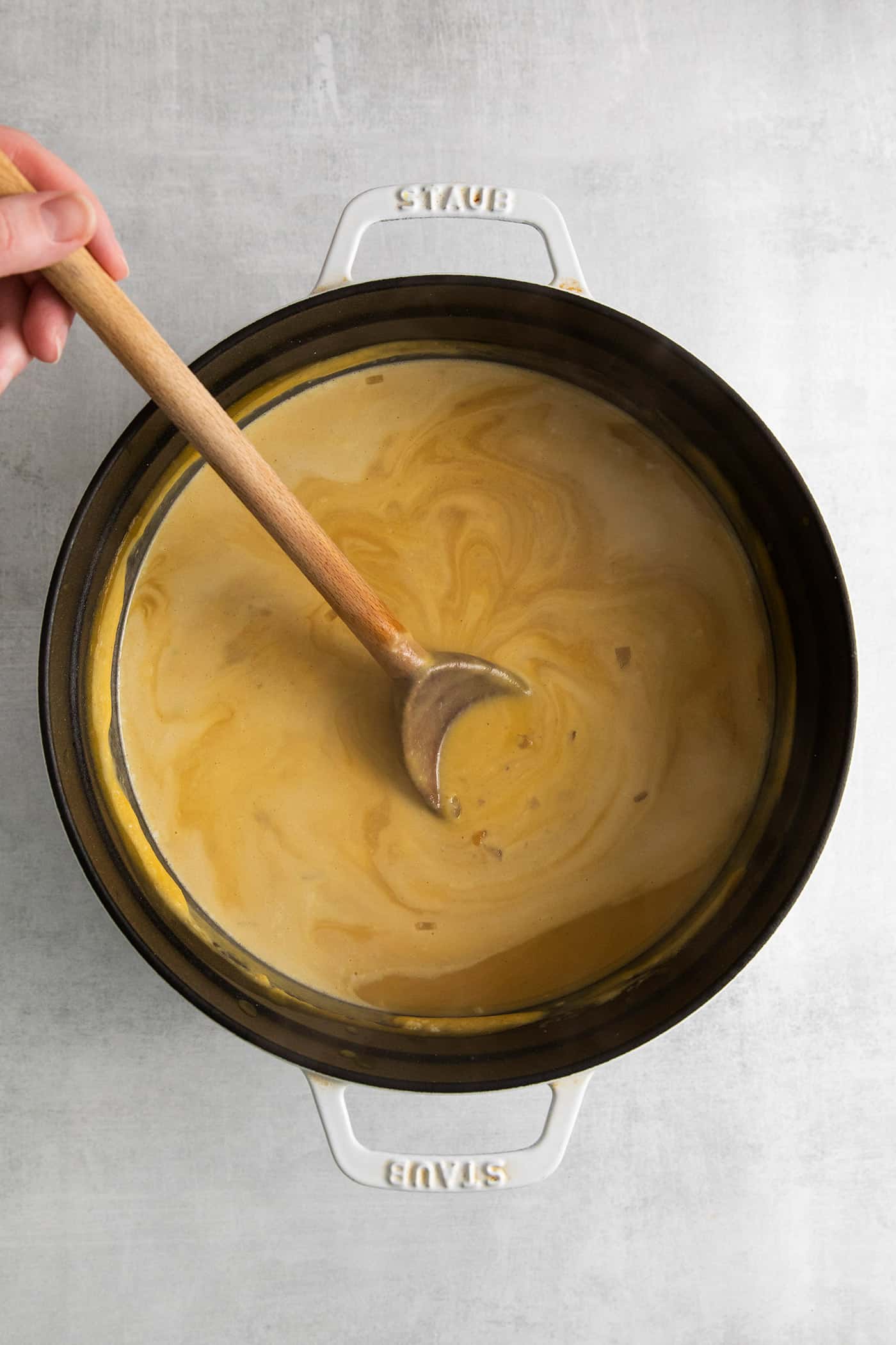 A wooden spoon stirring cream into squash soup