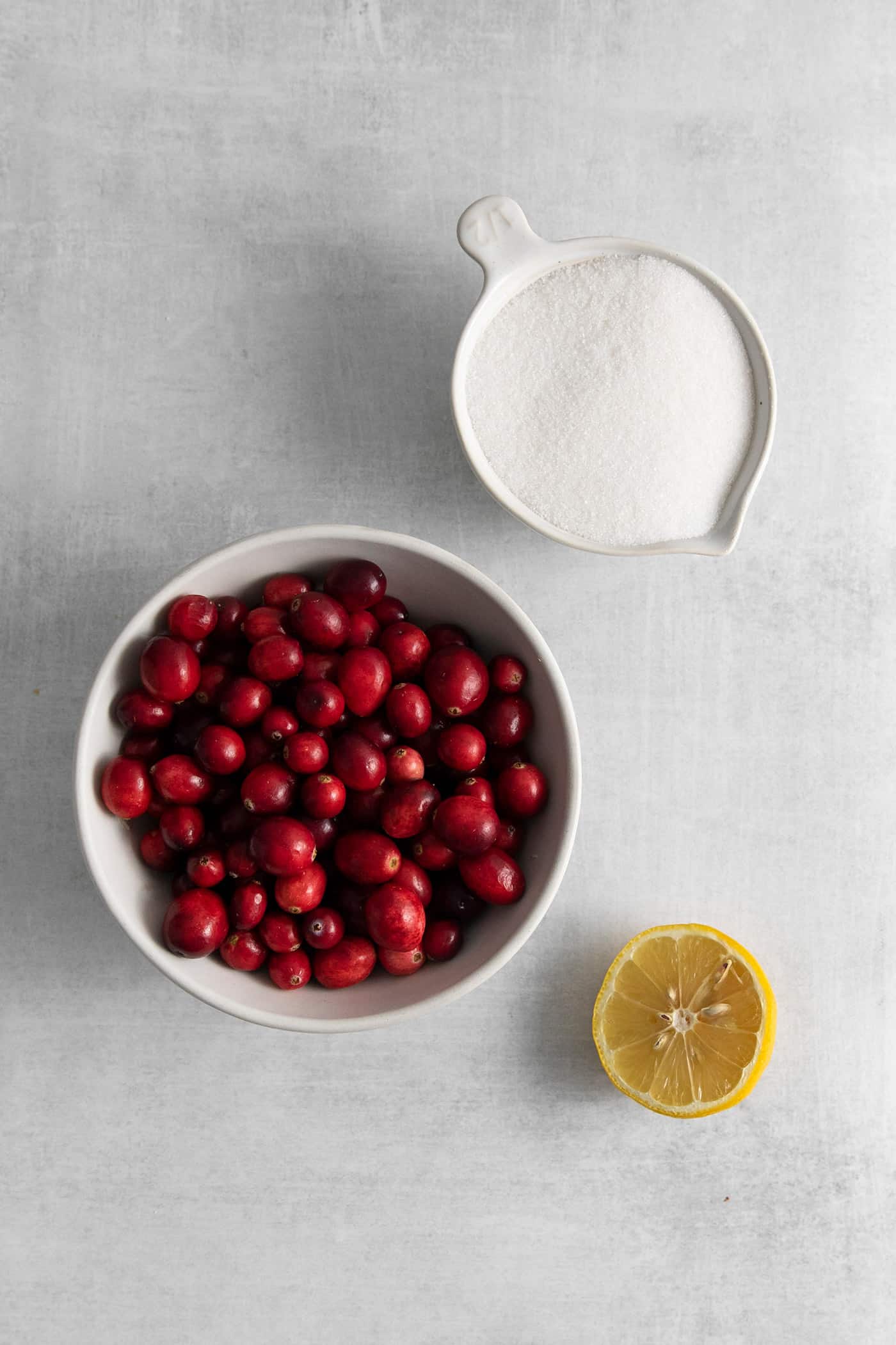 A bowl of cranberries, sugar, and half a lime