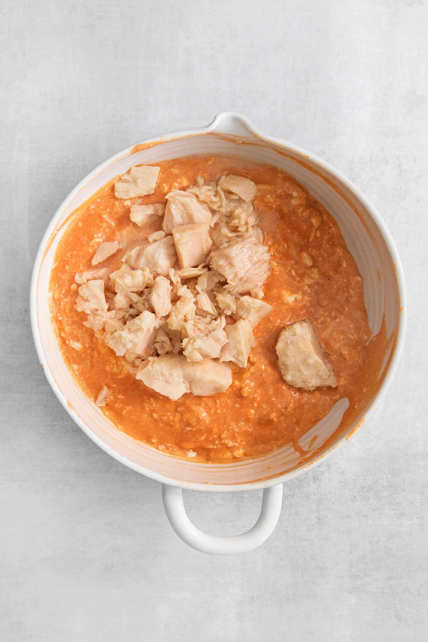 Canned chicken added to a bowl with hot sauce and cream cheese