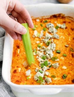 A hand dipping celery into buffalo chicken dip