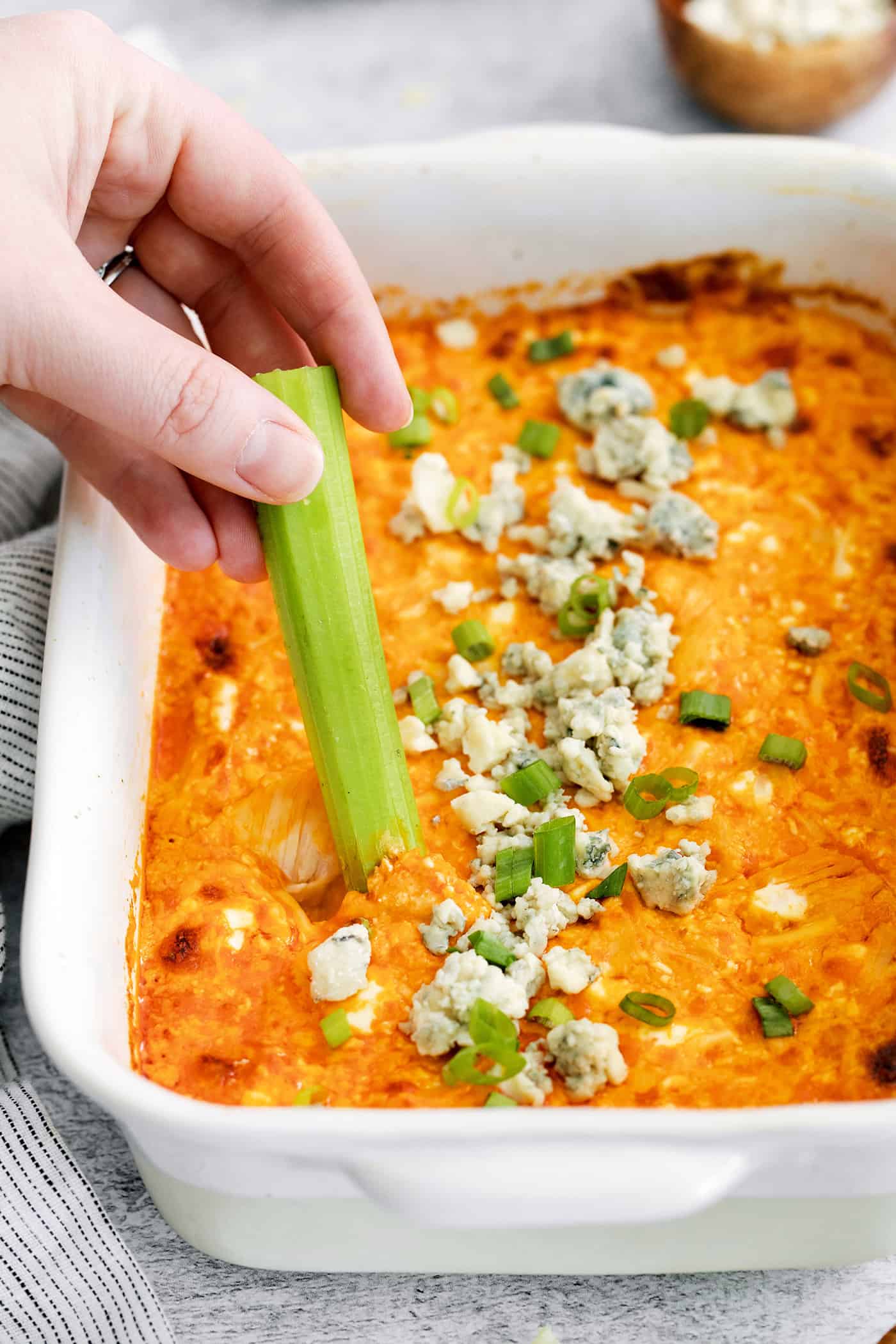 A hand dipping celery into buffalo chicken dip