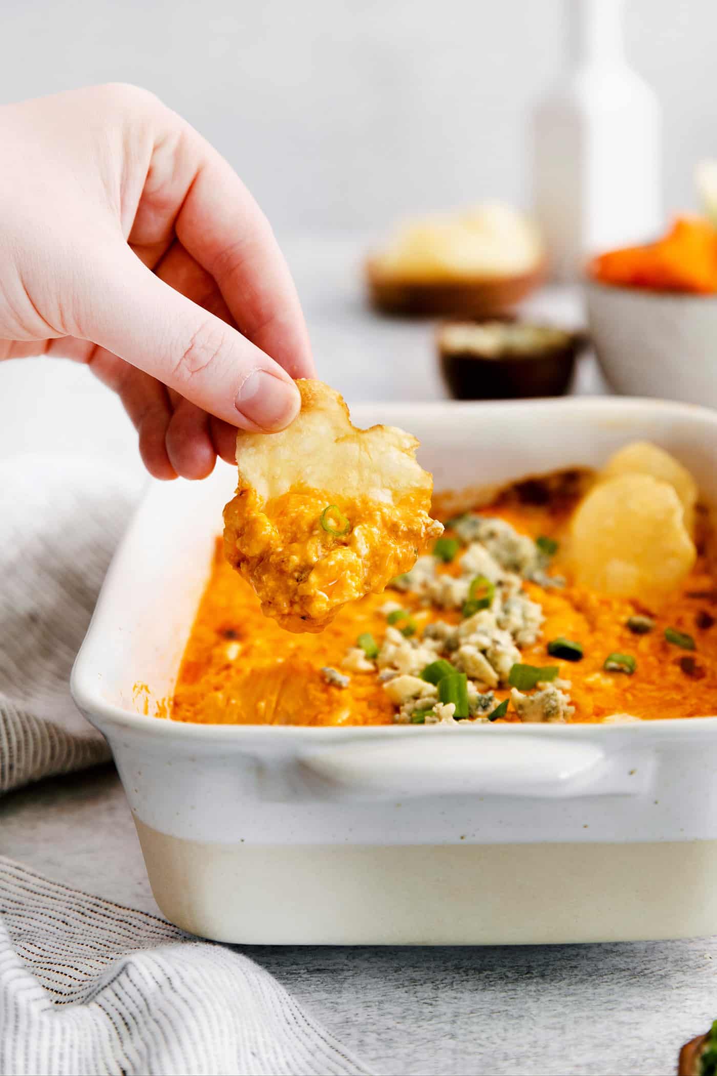 A hand using a tortilla chip to scoop some buffalo chicken dip