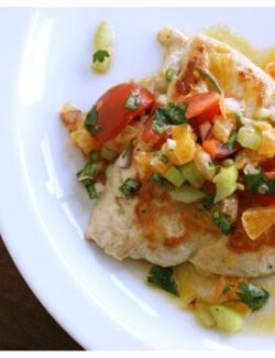 Chicken breast topped with clementine salsa on a white plate