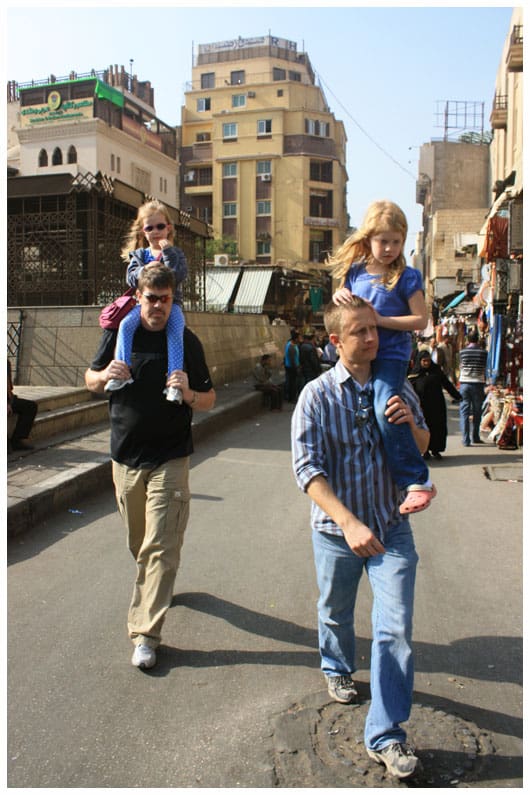 two men carrying their daughters on their backs