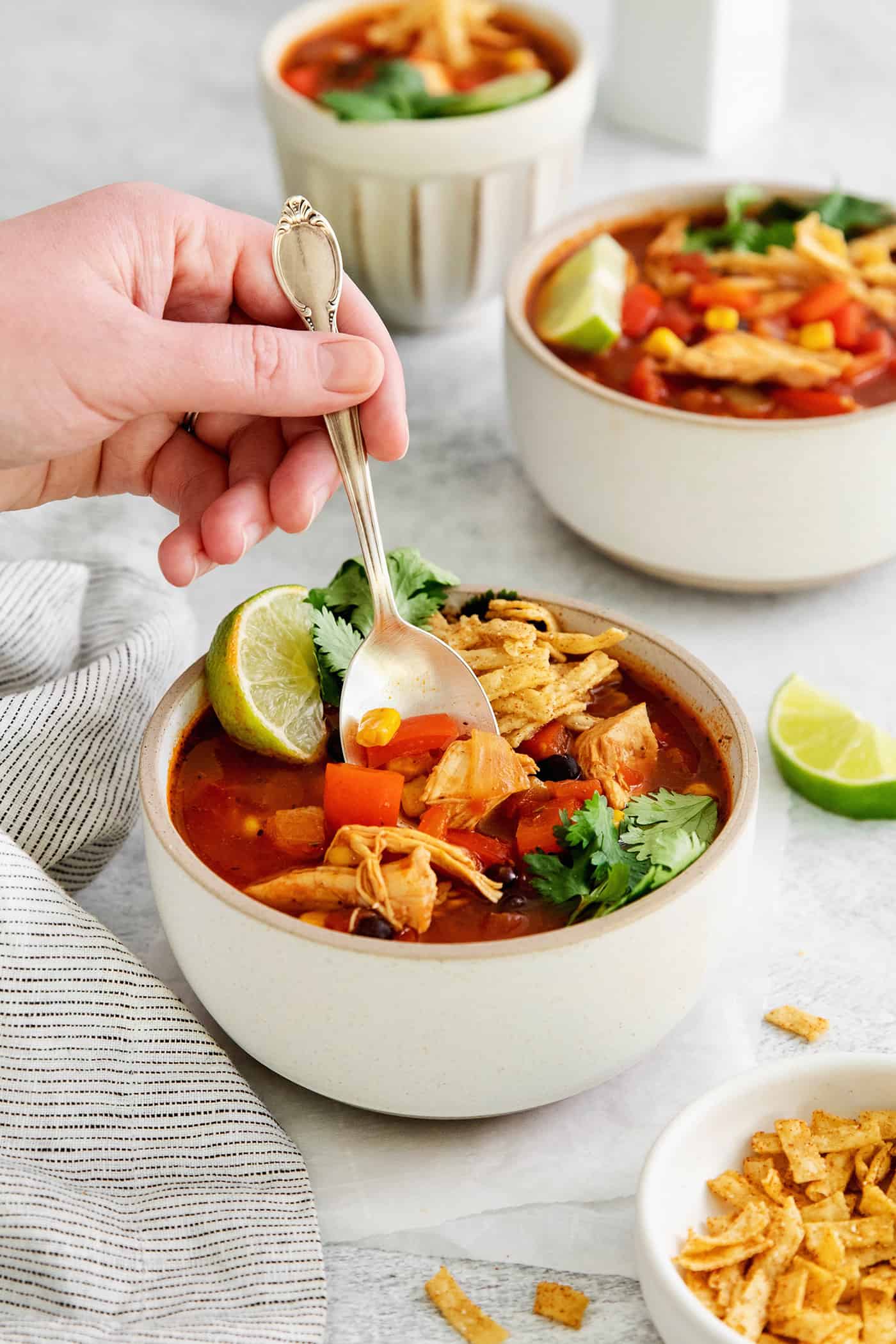 A hand holding a spoon in a bowl of chicken tortilla soup