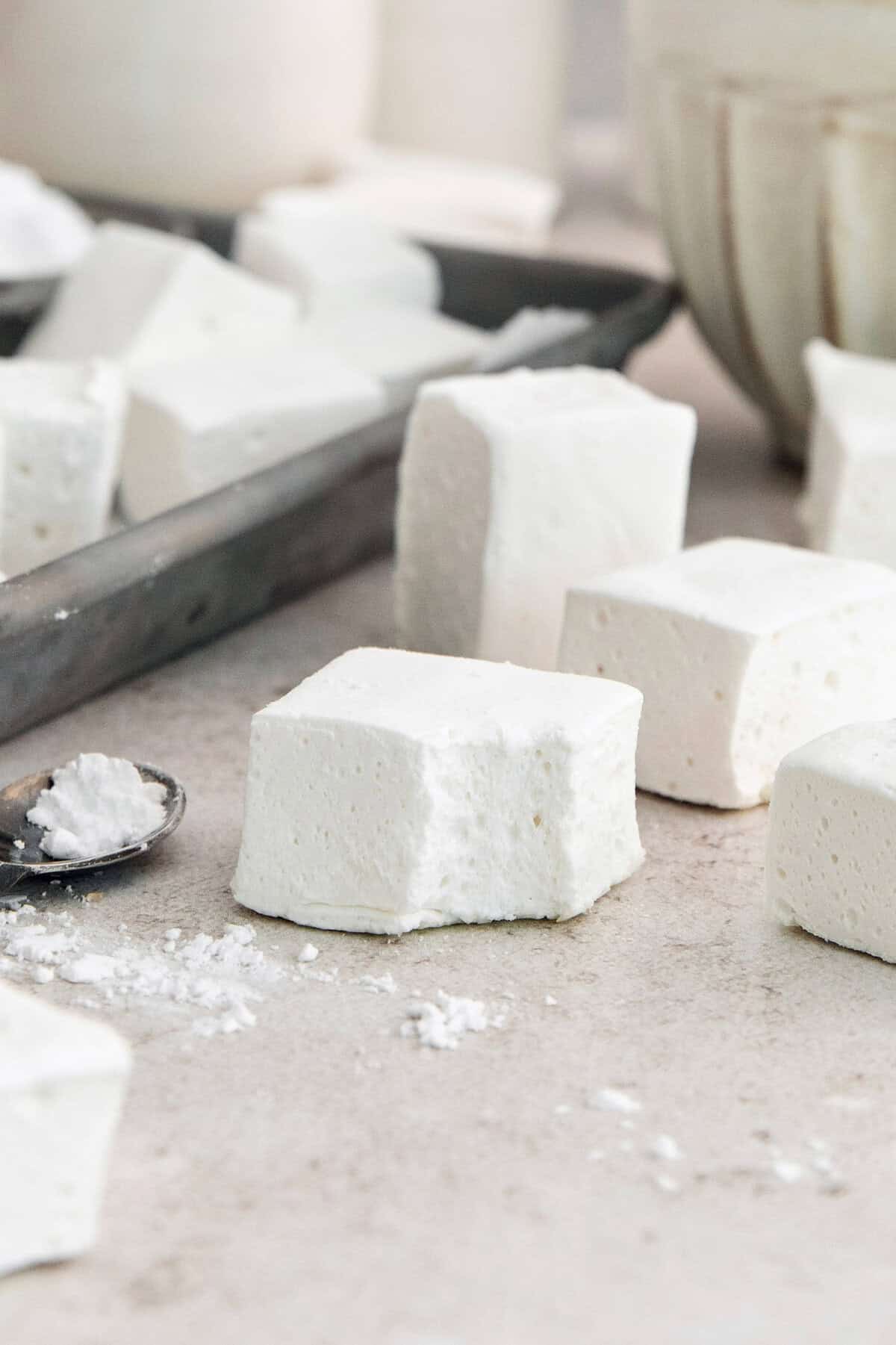 Fluffy homemade marshmallows on countertop, with one bitten into on the corner