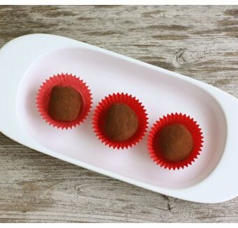 Top view of 3 chocolate truffles in baking cups on a white oval plate