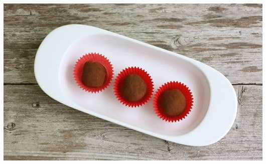Top view of 3 chocolate truffles in baking cups on a white oval plate