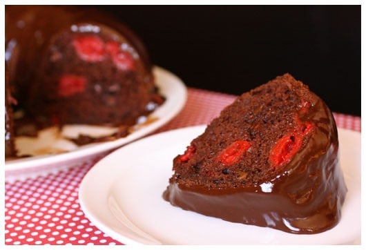 A slice of chocolate cherry bundt cake with chocolate glaze on a white plate