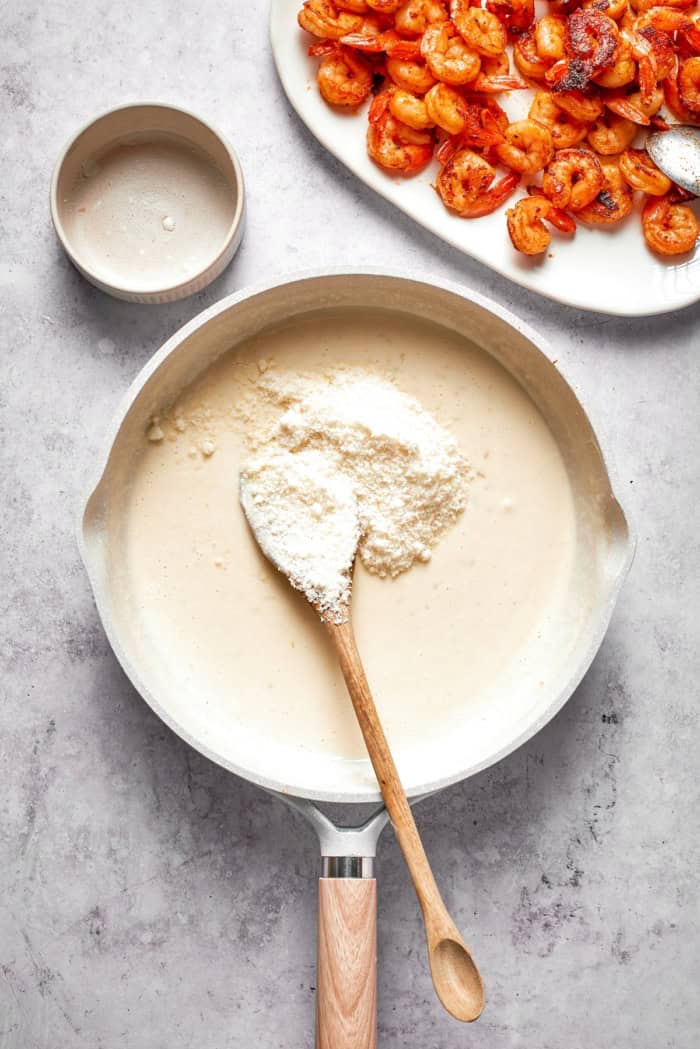 Parmesan cheese added to cream sauce in skillet.