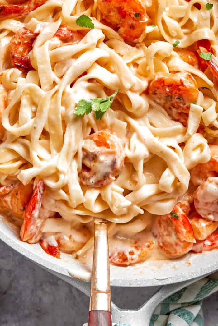 Creamy shrimp pasta in skillet with serving spoon.