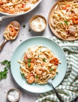Creamy shrimp pasta on 2 plates with skillet in background.