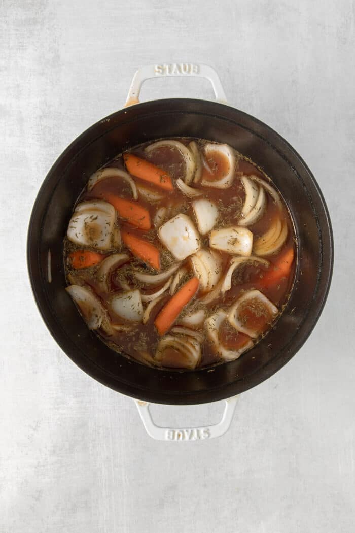 Overhead view of veggies and chuck roast in a pot with beef broth