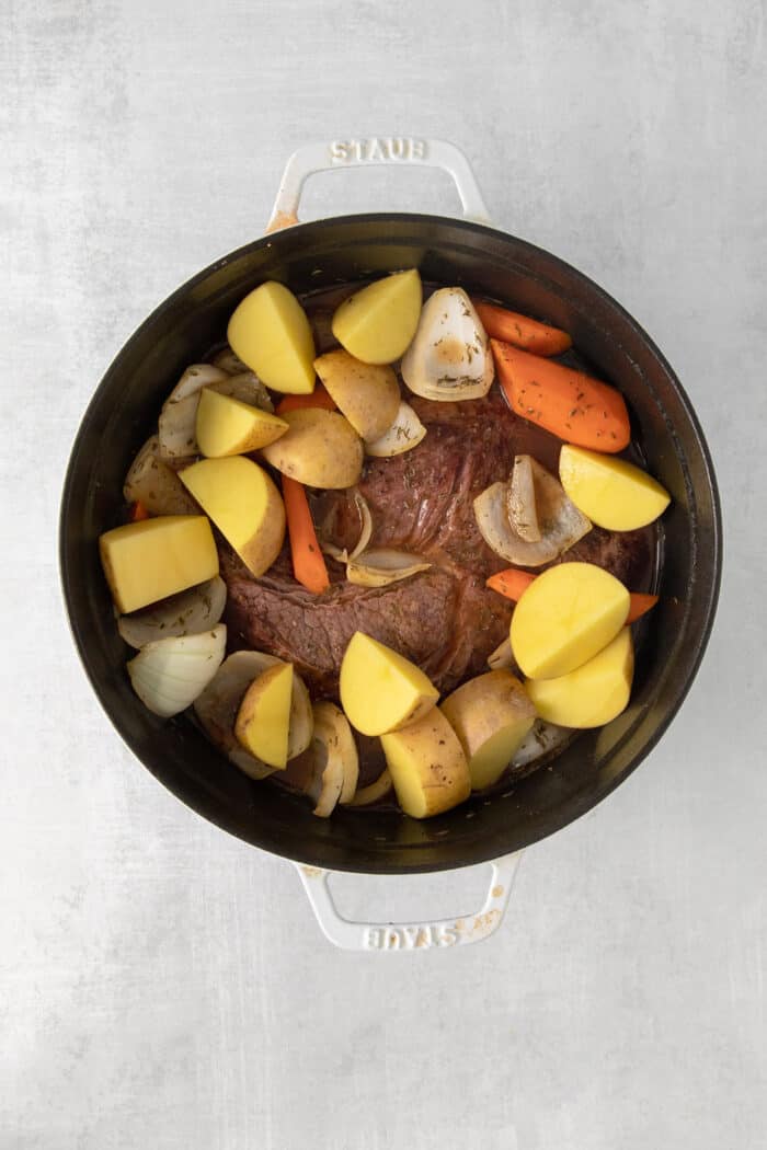 Potatoes on top of a chuck roast in a pot