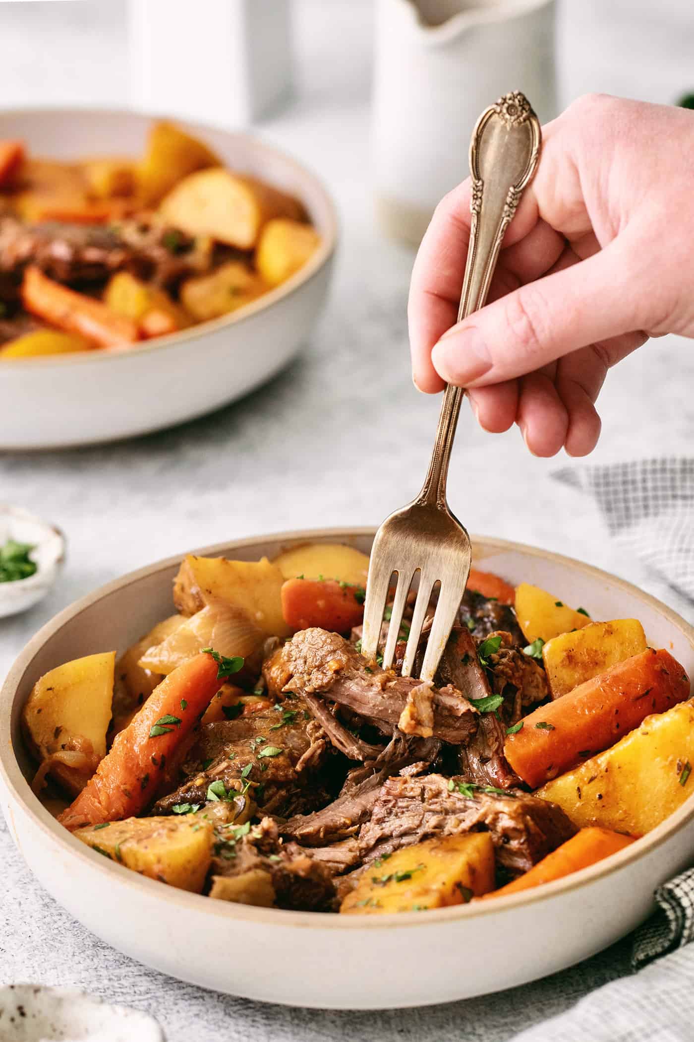 A fork diving into a piece of pot roast in a bowl