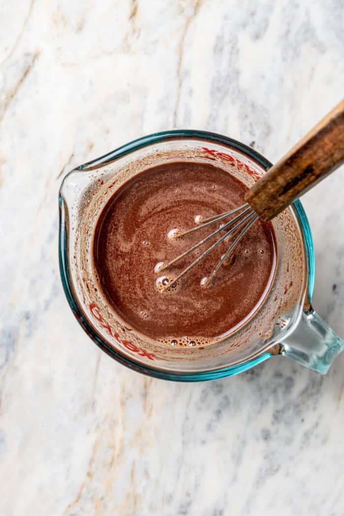 Overhead view of chocolate and water whisked in liquid measuring cup