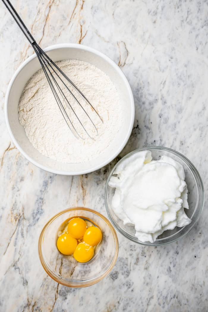 Overhead view of dry ingredients for German chocolate cake in bowl with bowls of whipped egg whites and egg yolks