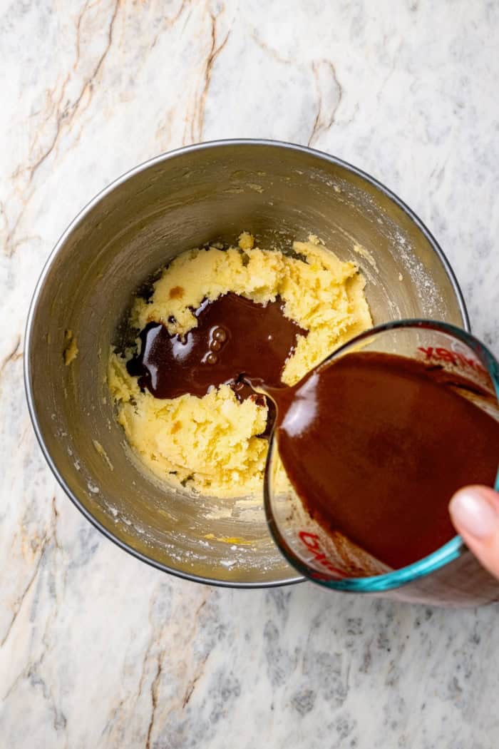 Pouring melted chocolate and water into creamed butter and sugar