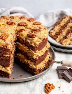 German chocolate cake on platter with one slice removed to show layers