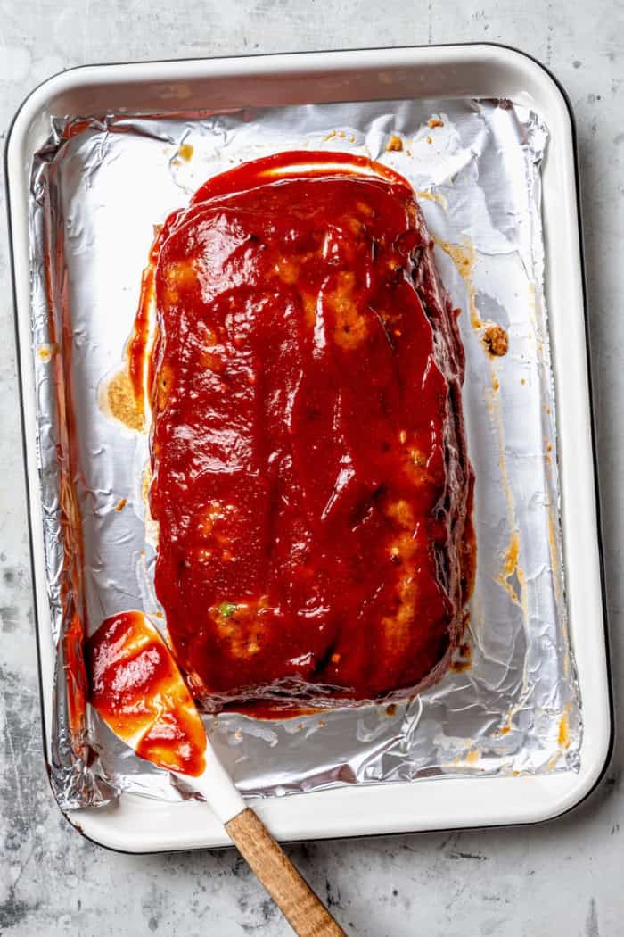 Spicy meatloaf sauce spread onto meatloaf on pan.