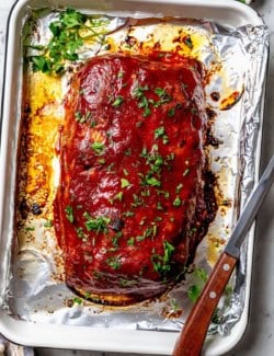 Spicy meatloaf on foil-lined sheet pan with parsley for garnish.