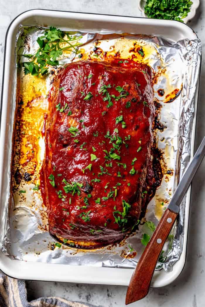 Spicy meatloaf on foil-lined sheet pan with parsley for garnish.