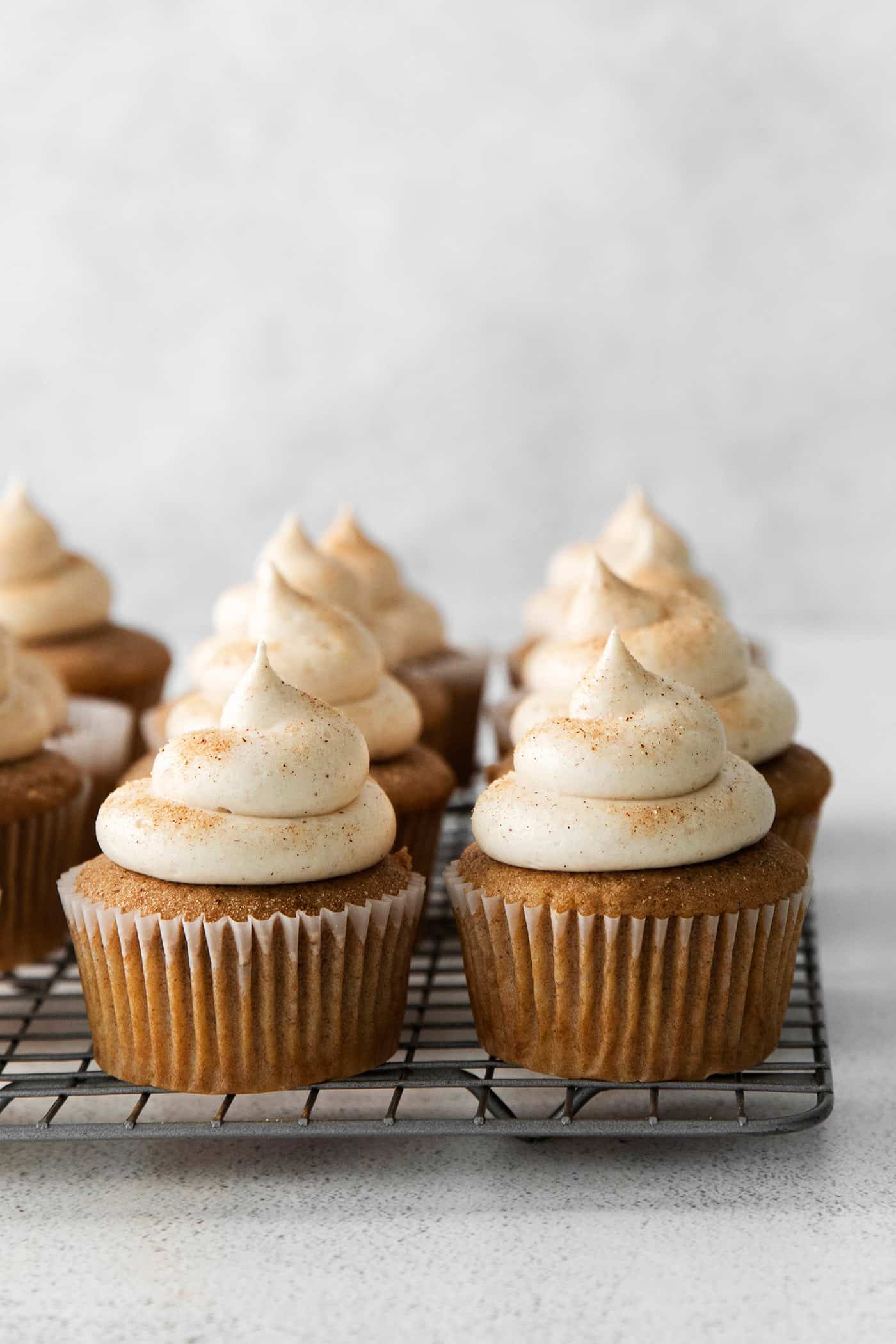 Snickerdoodle cupcakes with cream cheese frosting on a cooling 