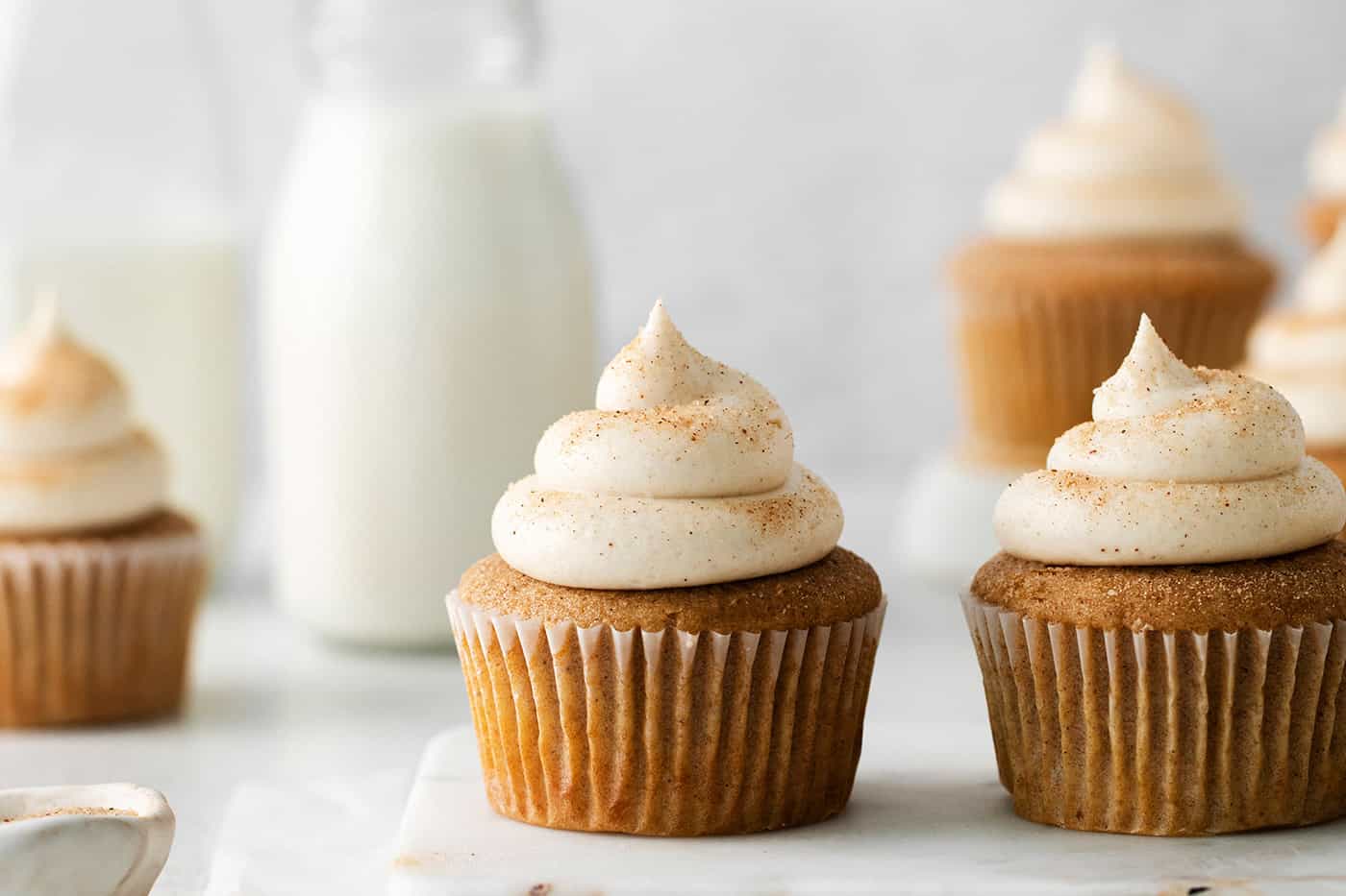 Snickerdoodle cupcakes with cream cheese frosting in front of a pitcher of milk