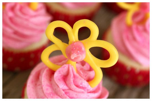 a yellow candy flower on top of a pink cupcake