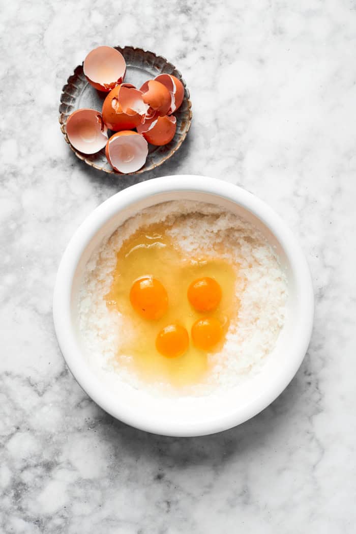 Overhead view of eggs added to sugar and oil in bowl