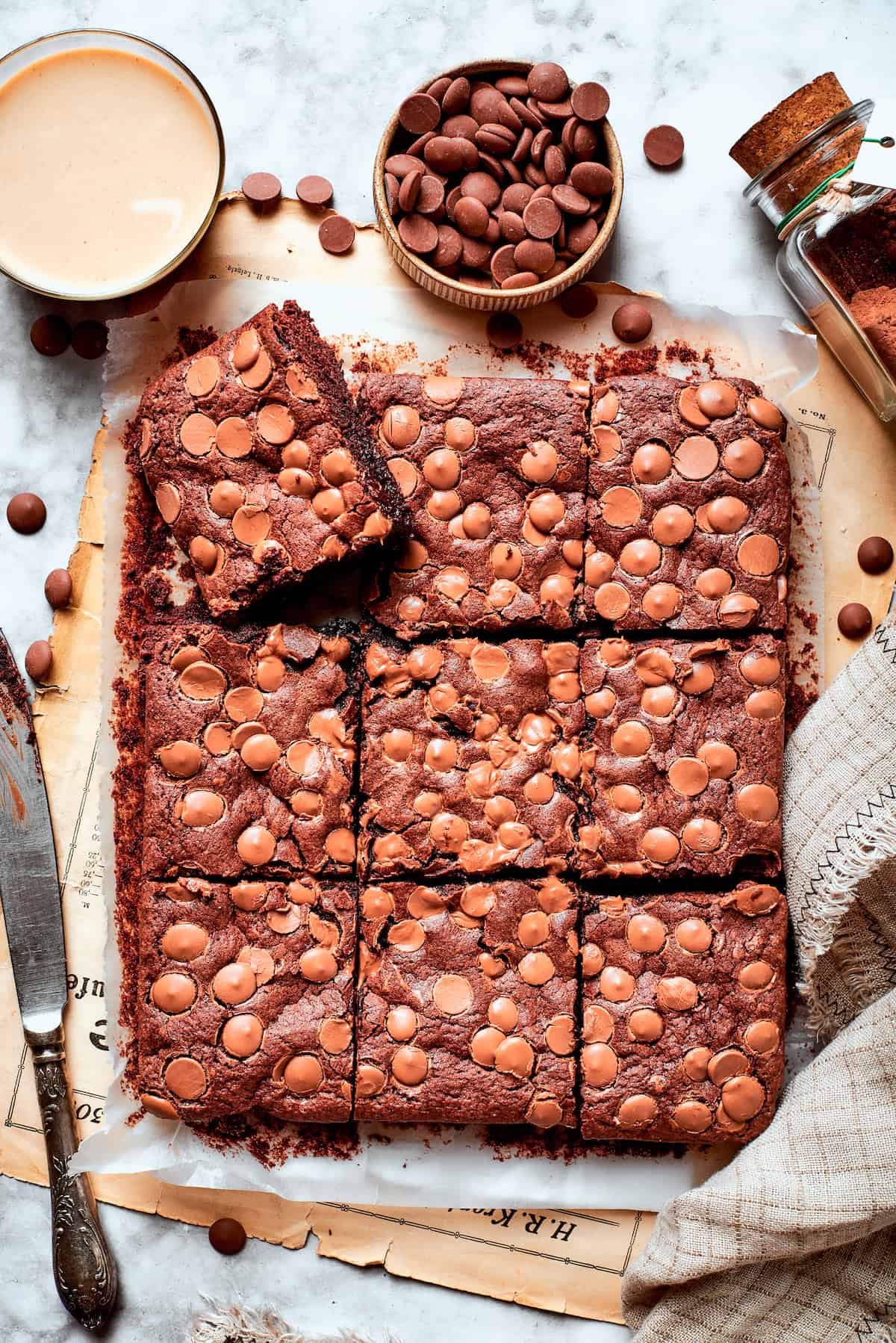 Overhead view of sliced fudgy brownies on parchment paper with bowl of chocolate chips