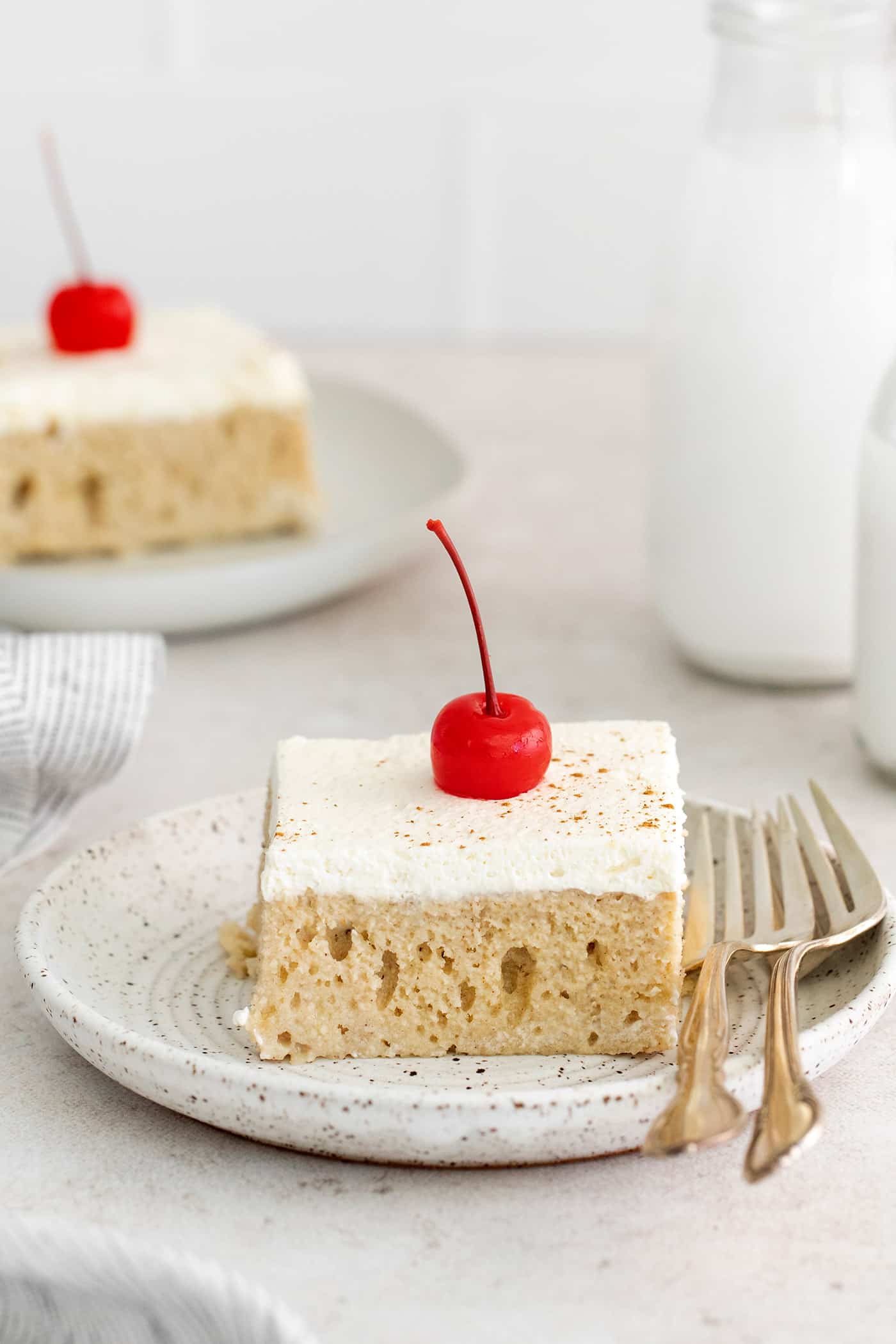 A slice of tres leche cake with a cherry on a plate