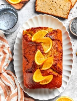 Loaf of orange glazed poppy seed bread on platter with orange slices on top.