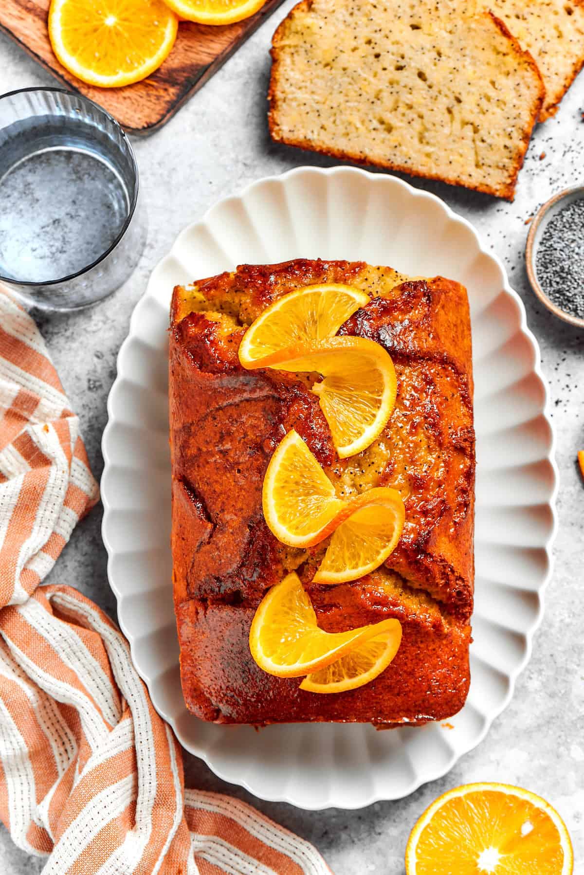 Loaf of orange glazed poppy seed bread on platter with orange slices on top.