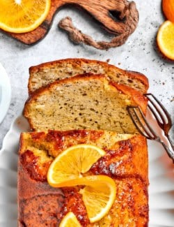 Tongs picking up slice of orange glazed poppy bread from loaf.