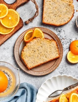 Slice of orange poppy seed bread on plate set next to another slice on countertop.