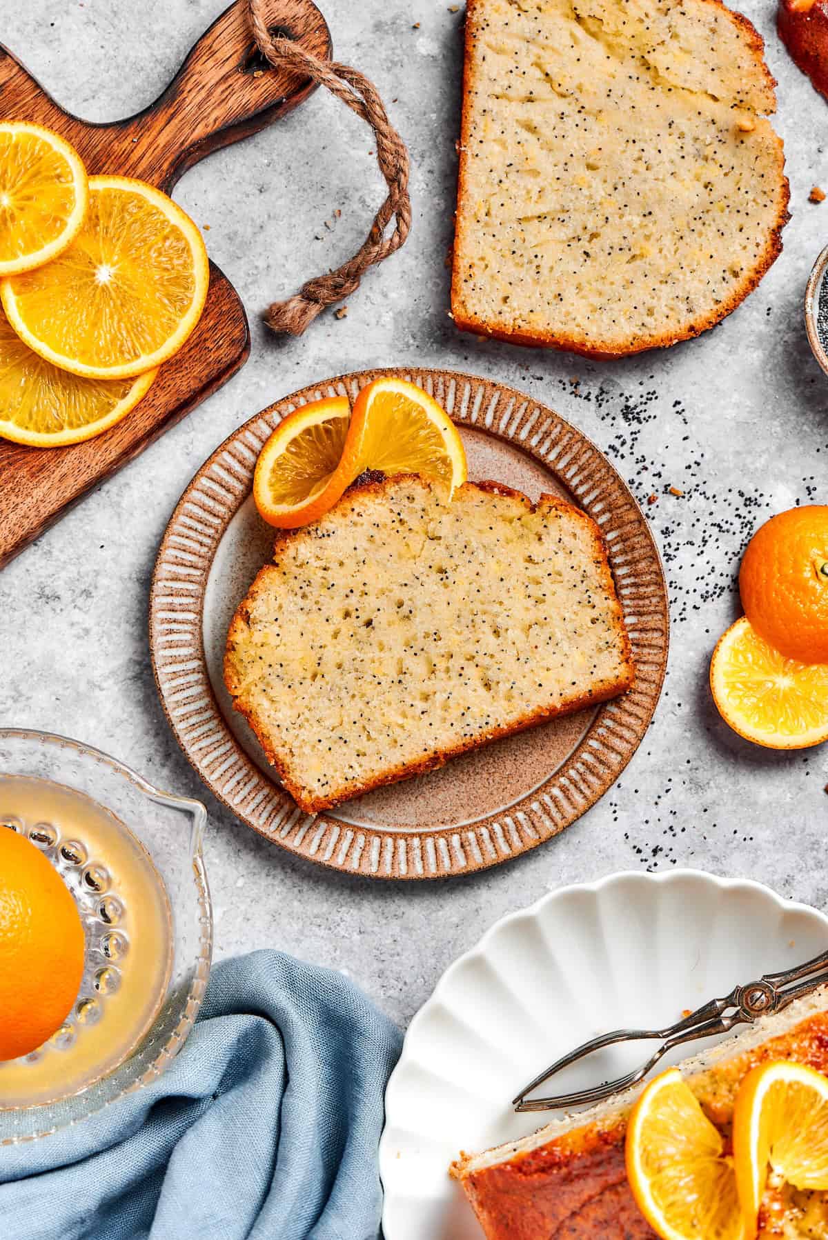 Slice of orange poppy seed bread on plate set next to another slice on countertop.