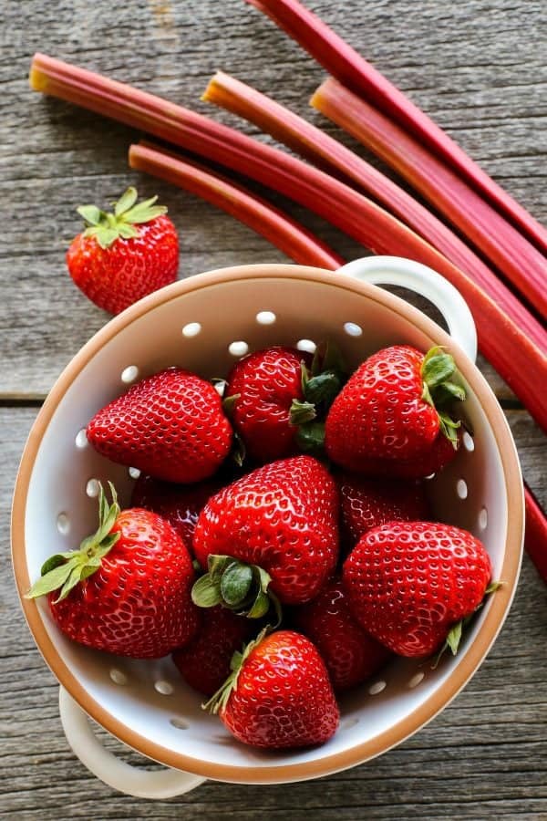 strawberries in a colander and stalks of rhubarb