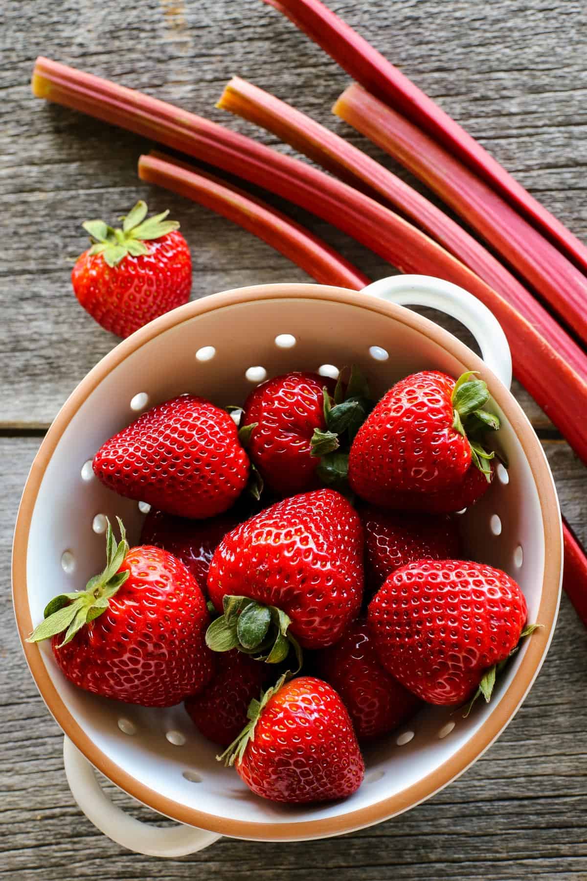 strawberries in a colander and stalks of rhubarb