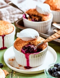 Spoon digging into mini blueberry cobbler topped with scoop of ice cream.