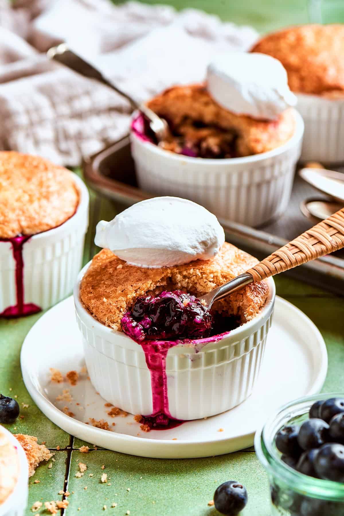 Spoon digging into mini blueberry cobbler topped with scoop of ice cream.